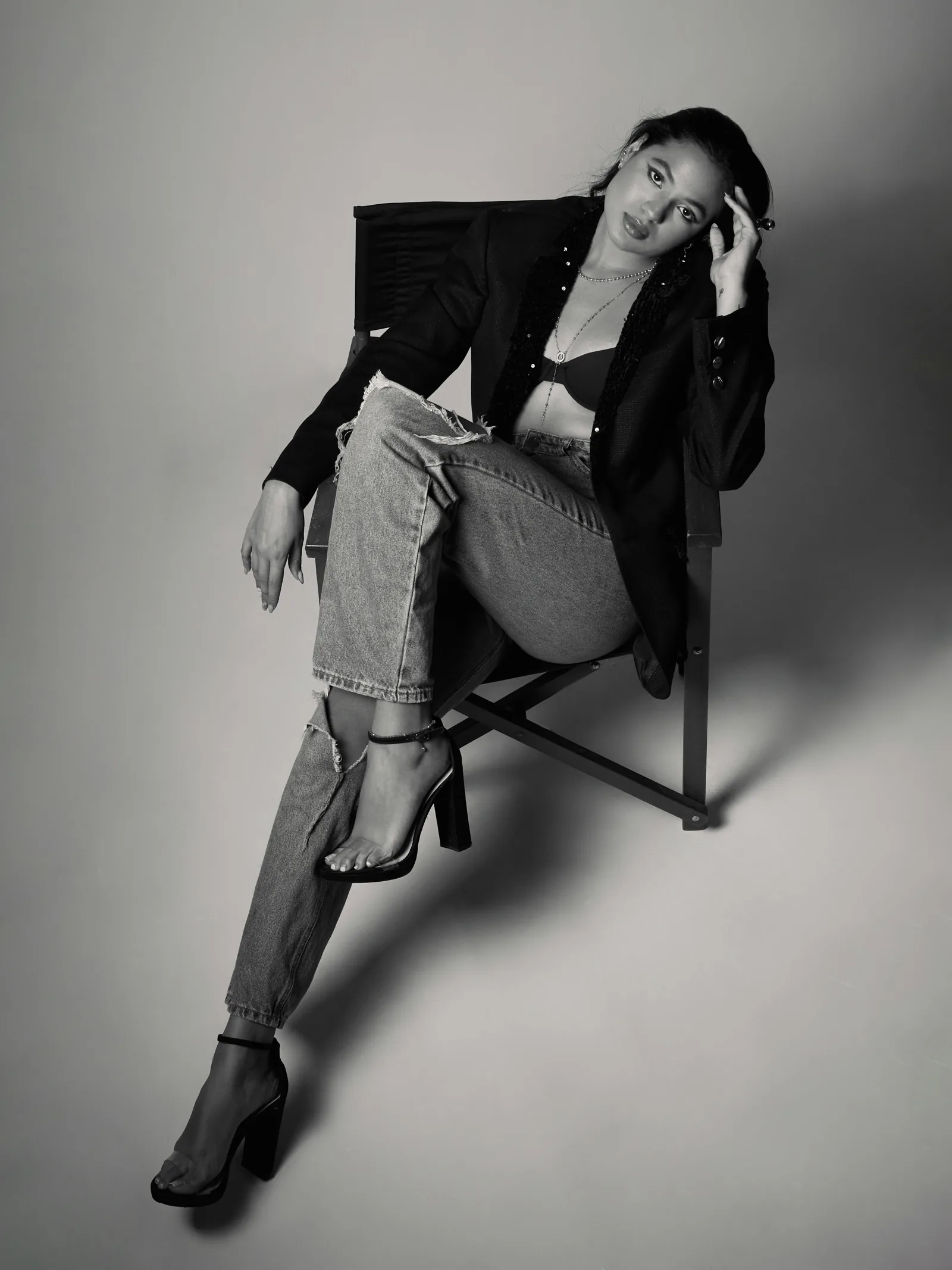 Black and white editorial fashion photograph of a model seated on a chair